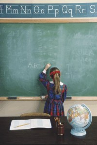 Une jeune écolière écrit au tableau noir.