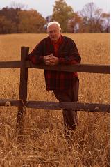 Un homme plus âgé se tient contre une clôture dans un champ doré d’automne.